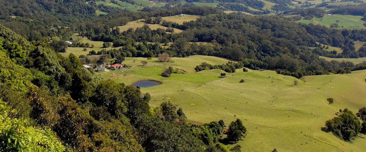 A panoramic view of rolling hills, a small pond, and scattered buildings in a rural landscape.