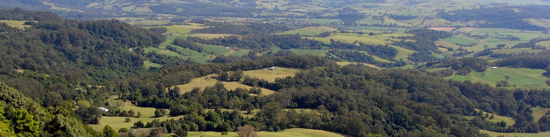 A panoramic view of rolling hills, a small pond, and scattered buildings in a rural landscape.