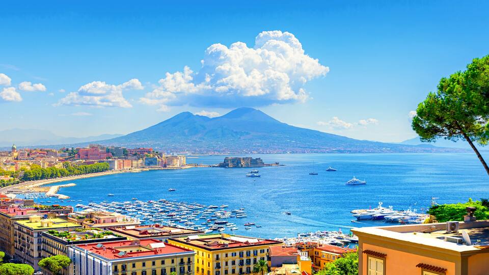 Naples, Italy. View of the Gulf of Naples from the Posillipo hill with Mount Vesuvius far in the background and some pine trees in foreground. Banner header horizontal image. 2021-08-31.