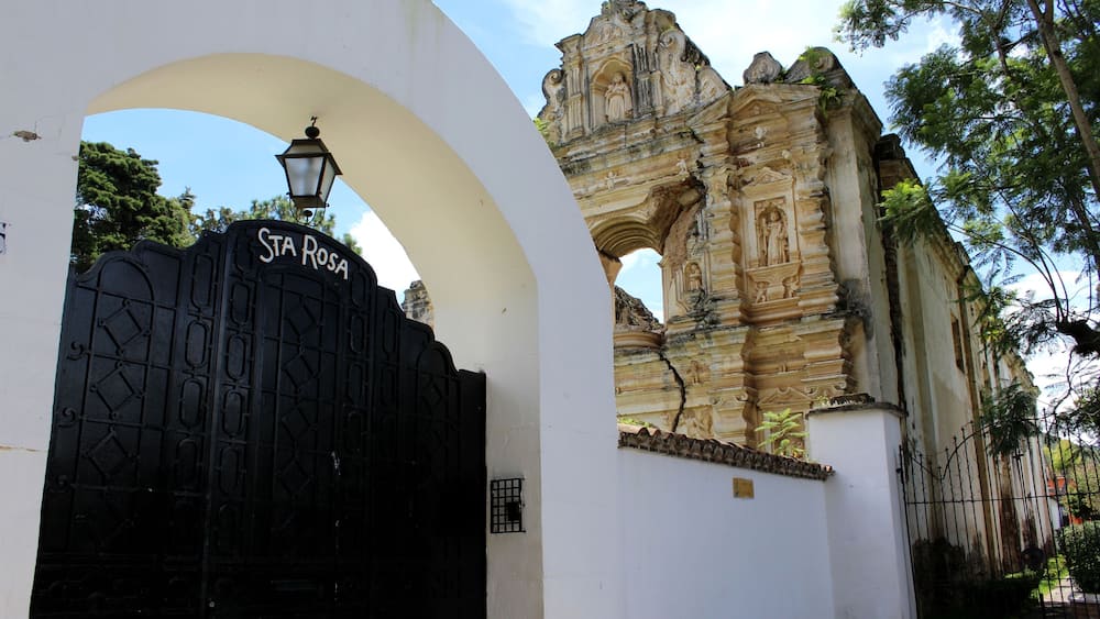 La chiesa Santa Rosa da Lima con il suo portone nero incorniciato da un muro bianco e sul lato enormi alberi. Antigua, Guatemala