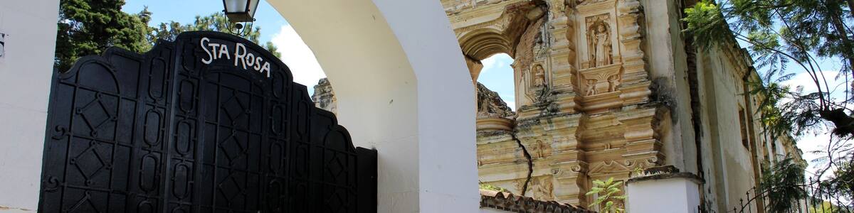 La chiesa Santa Rosa da Lima con il suo portone nero incorniciato da un muro bianco e sul lato enormi alberi. Antigua, Guatemala