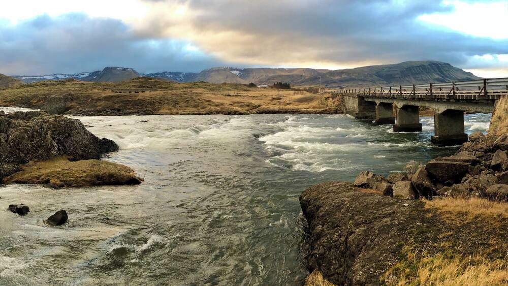 A river with a bridge, rocky terrain, and distant mountains.
