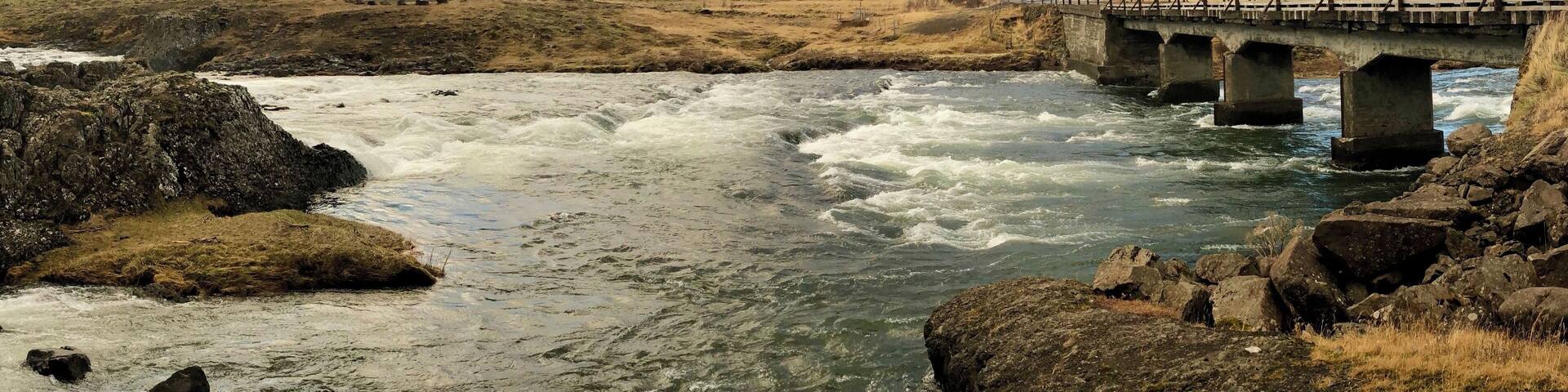 A river with a bridge, rocky terrain, and distant mountains.