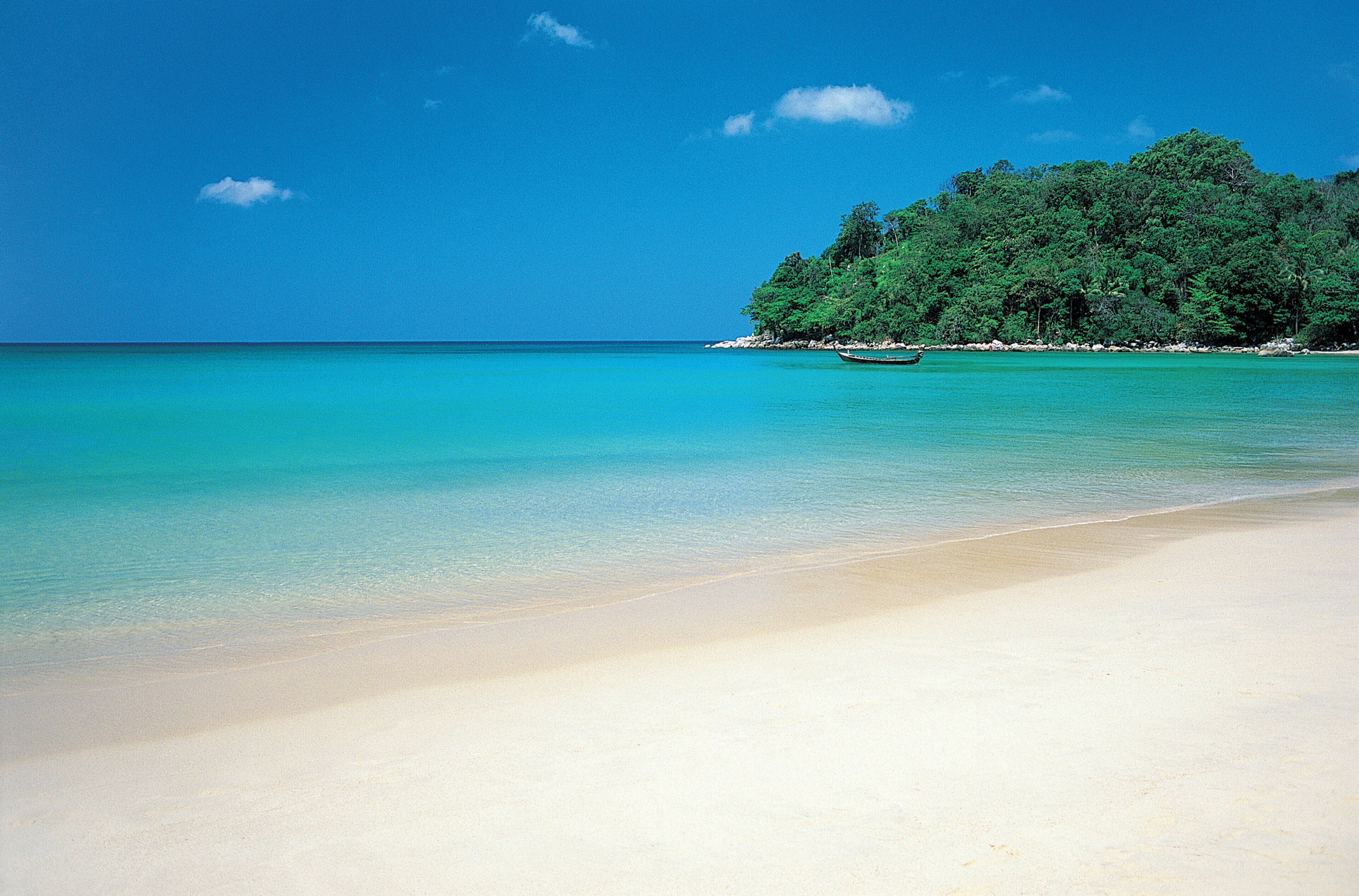 Uma praia com águas turquesa cristalinas, areal arenoso e uma ilha arborizada ao fundo.