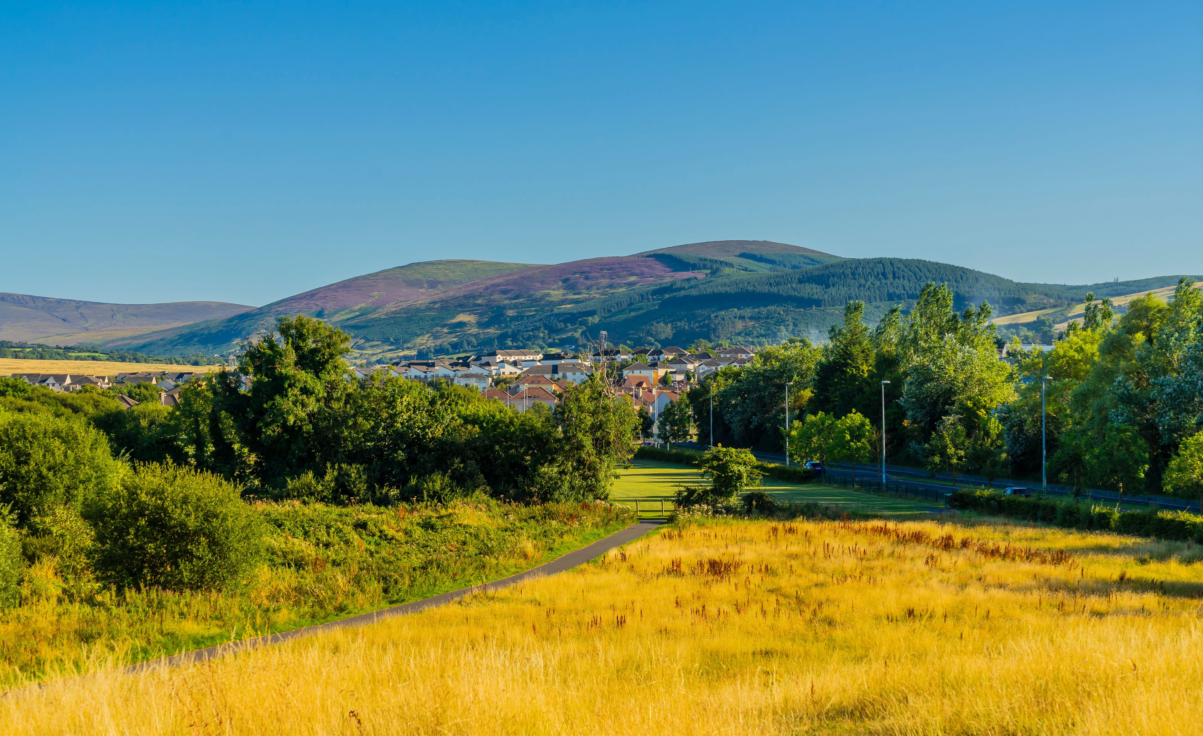 A rural landscape with a village, rolling hills, and a clear sky.