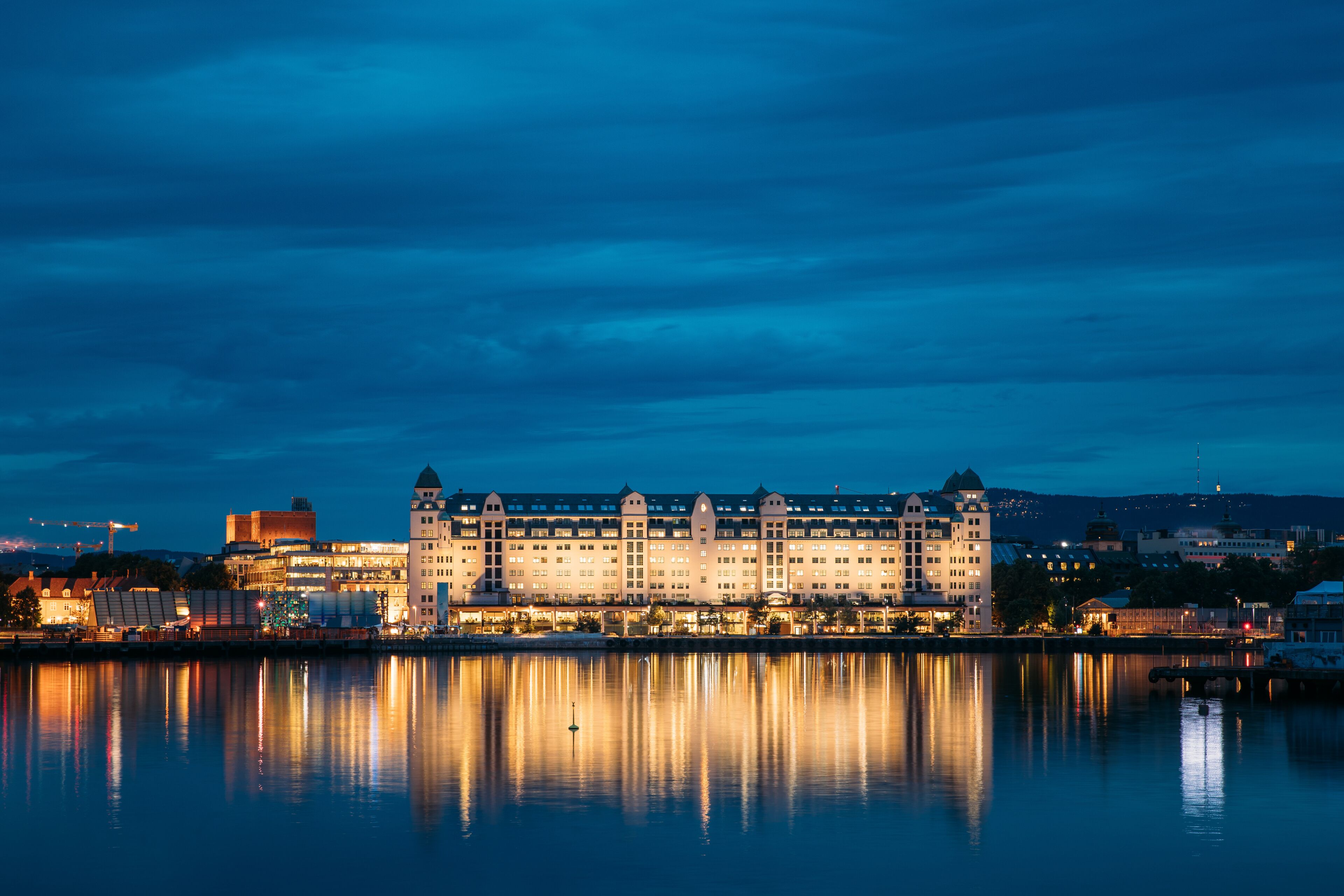A large, illuminated hotel by a calm body of water at night.