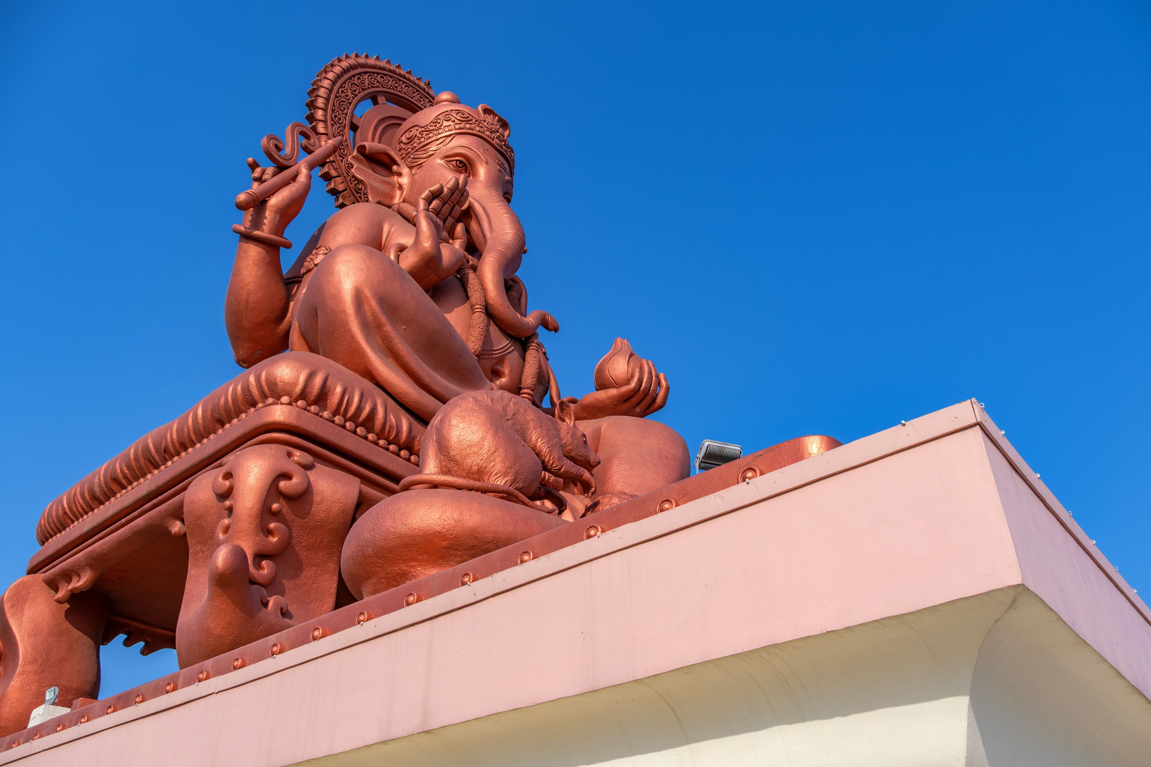 A large bronze statue of a deity with intricate carvings, set against a clear blue sky.