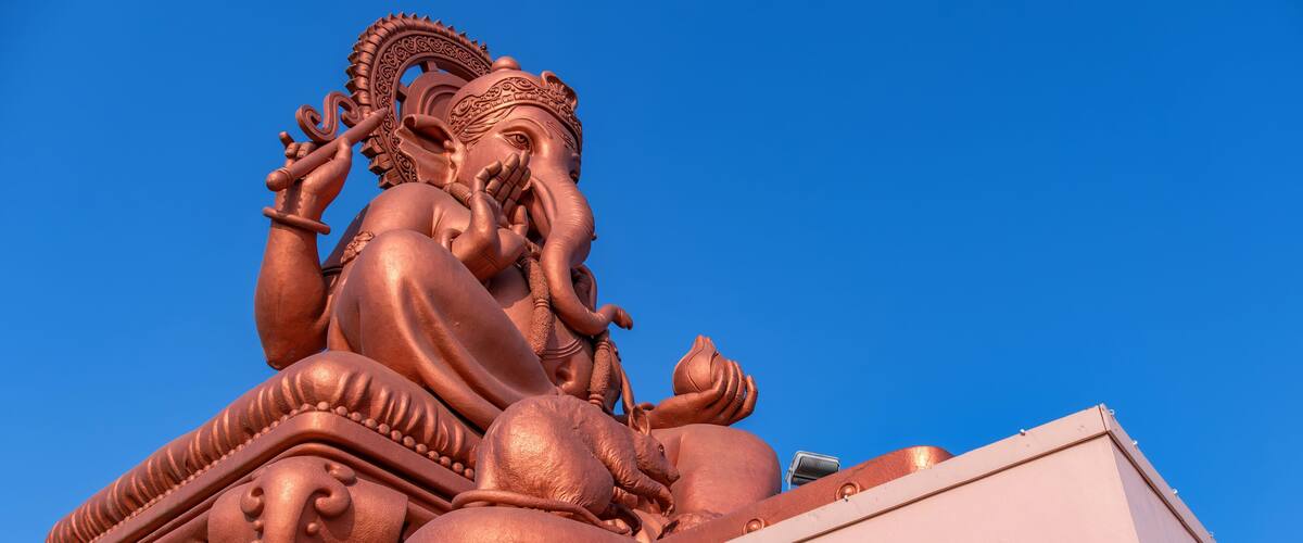 A large bronze statue of a deity with intricate carvings, set against a clear blue sky.