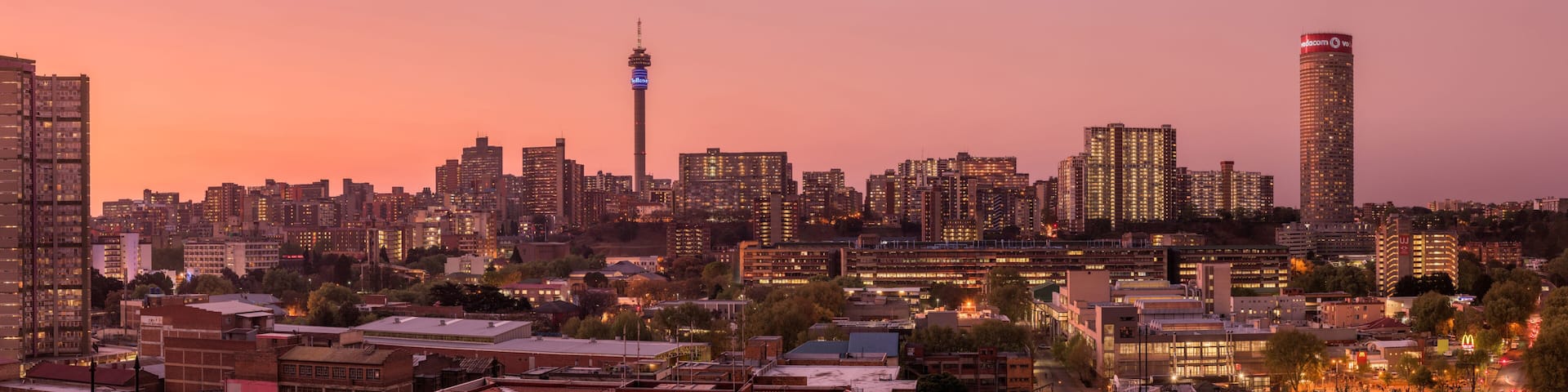 A city skyline at dusk with illuminated buildings, a prominent tower, and a clear sky.