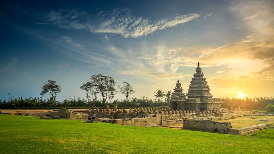 A temple complex with a large stupa and surrounding ruins, set against a sunset sky.