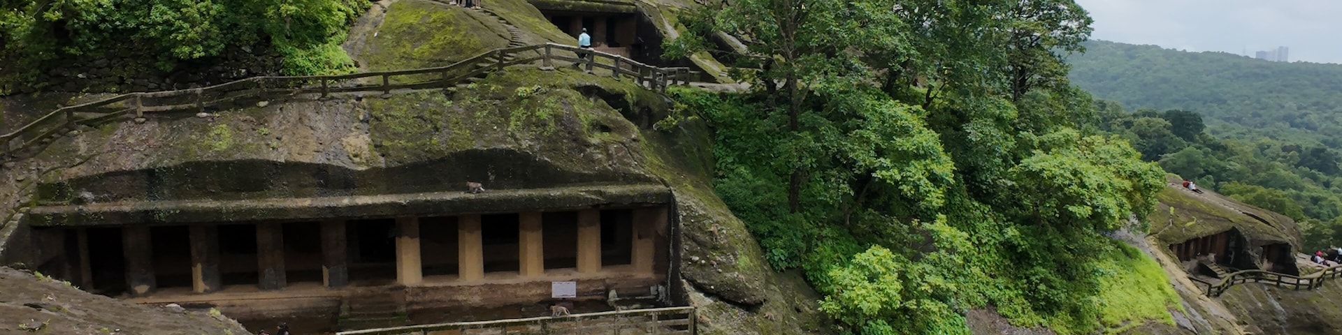 A historical site with ancient stone structures, a staircase leading up to a platform, and lush greenery.