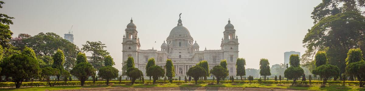 A large, historic building with two domes and two towers, surrounded by a pond and trees.