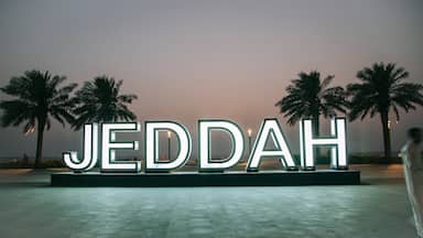 Illuminated letters spelling "JEDDAH" on a platform with palm trees in the background.