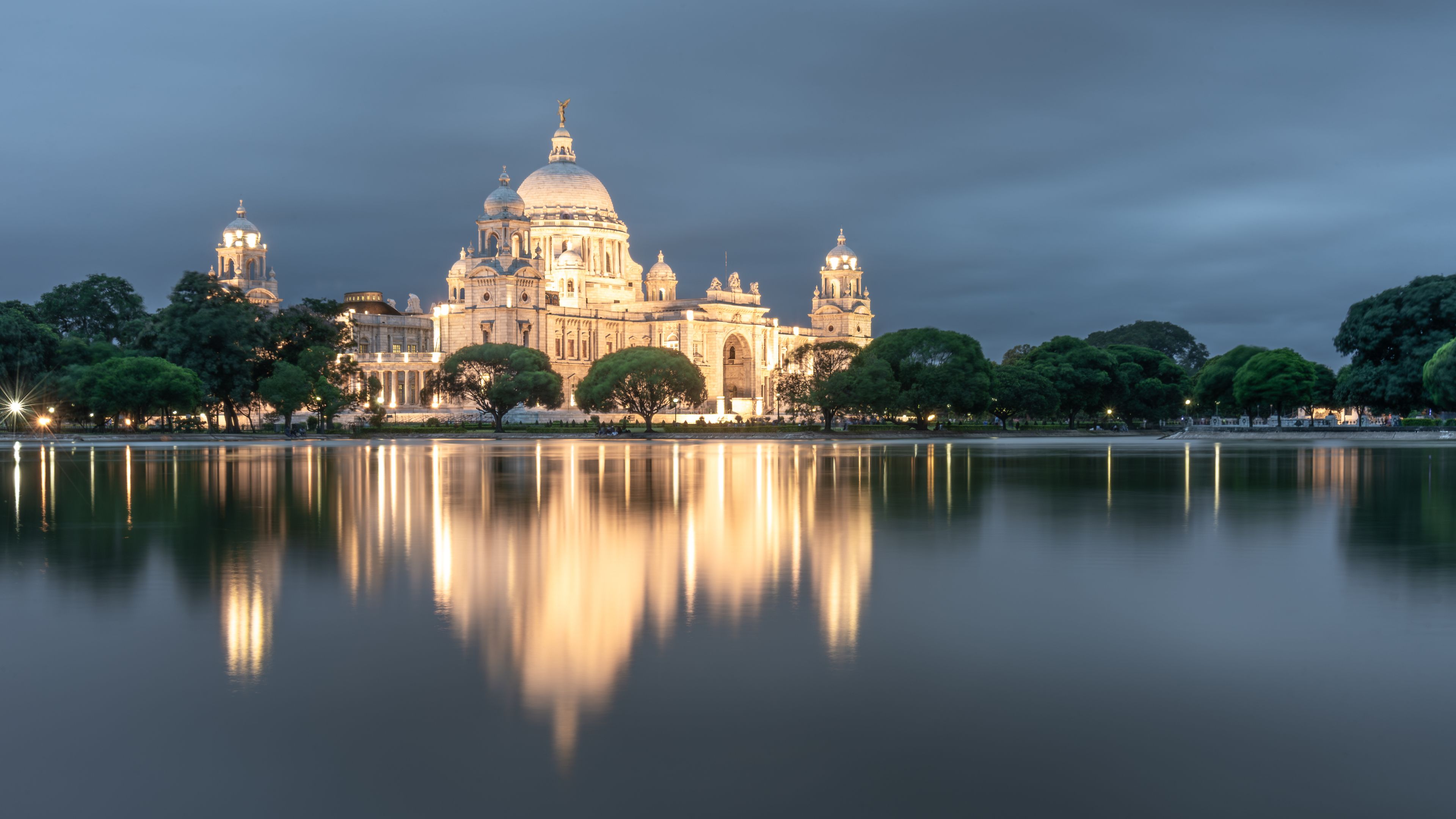 A grand, illuminated cathedral with a large dome, reflecting on a calm lake.