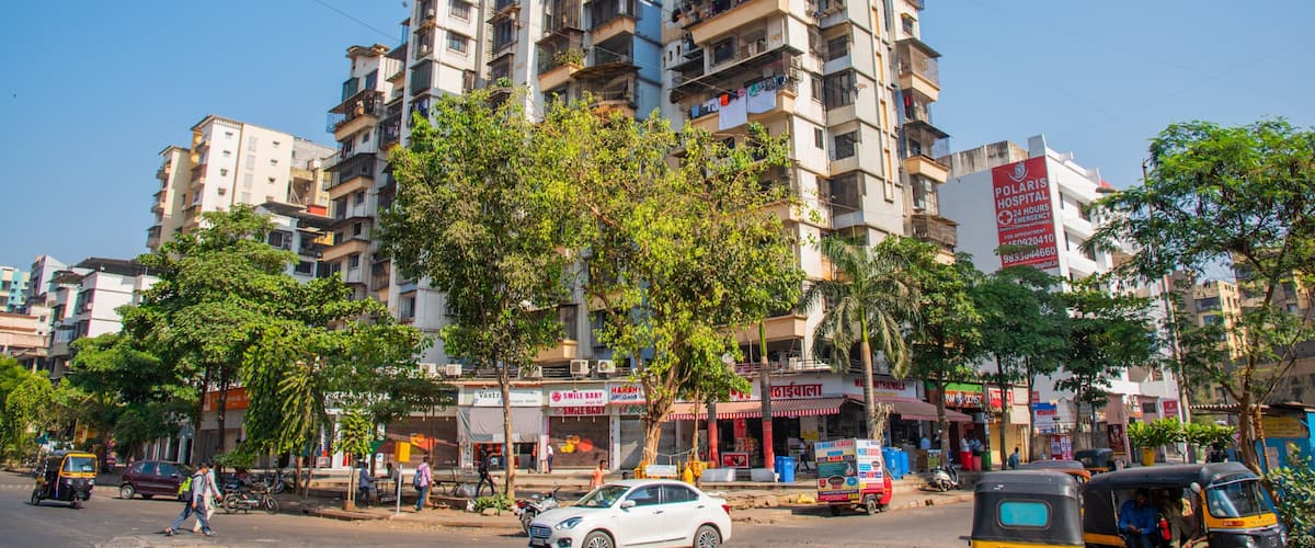 A multi-story building with balconies, a street with pedestrians, and auto-rickshaws.