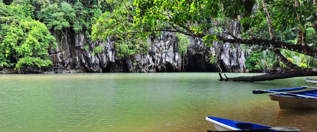 A calm river with clear water, surrounded by lush greenery and rocky cliffs.