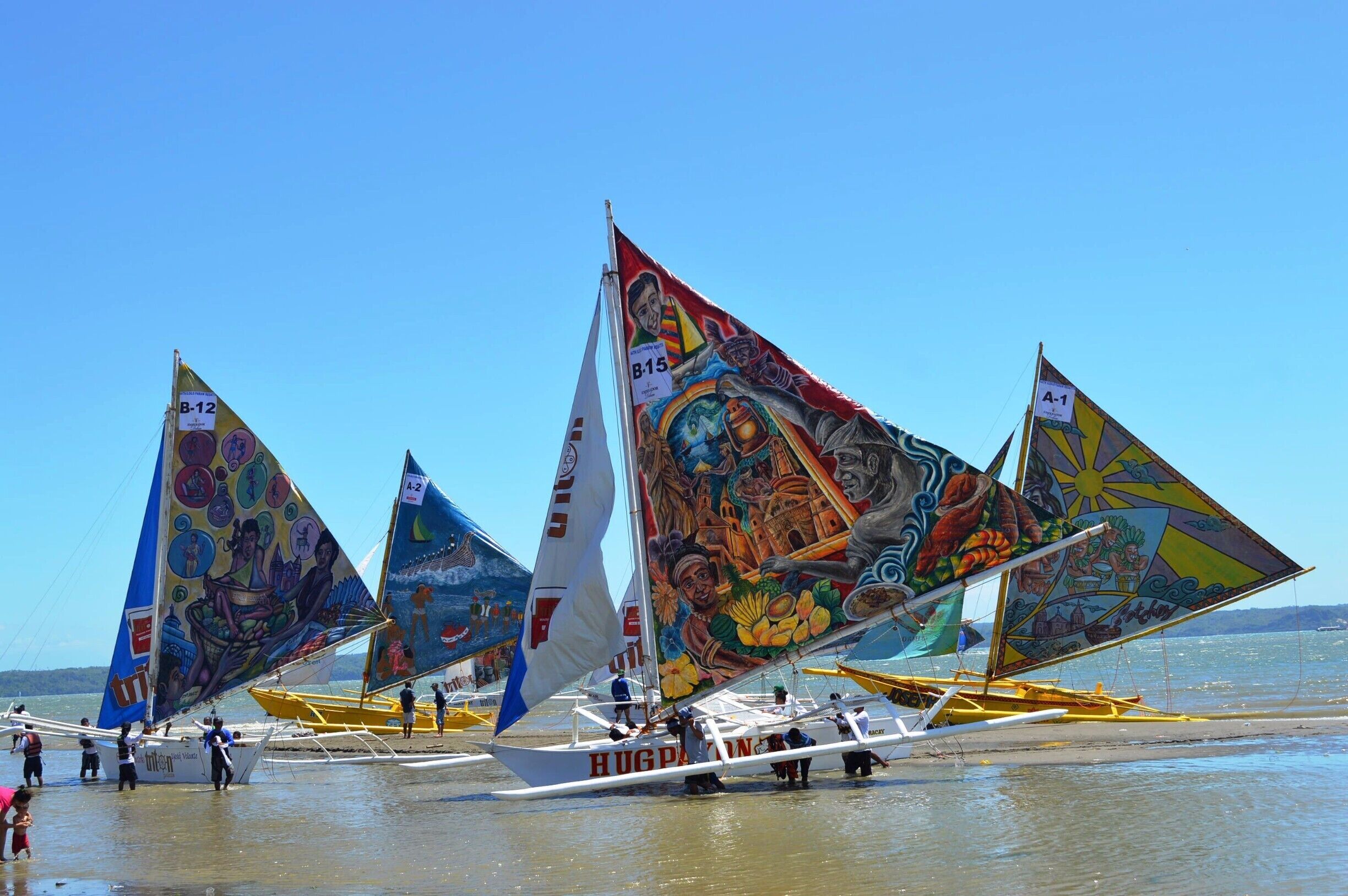 Colorful sailboats with intricate designs on their sails, docked on a beach.
