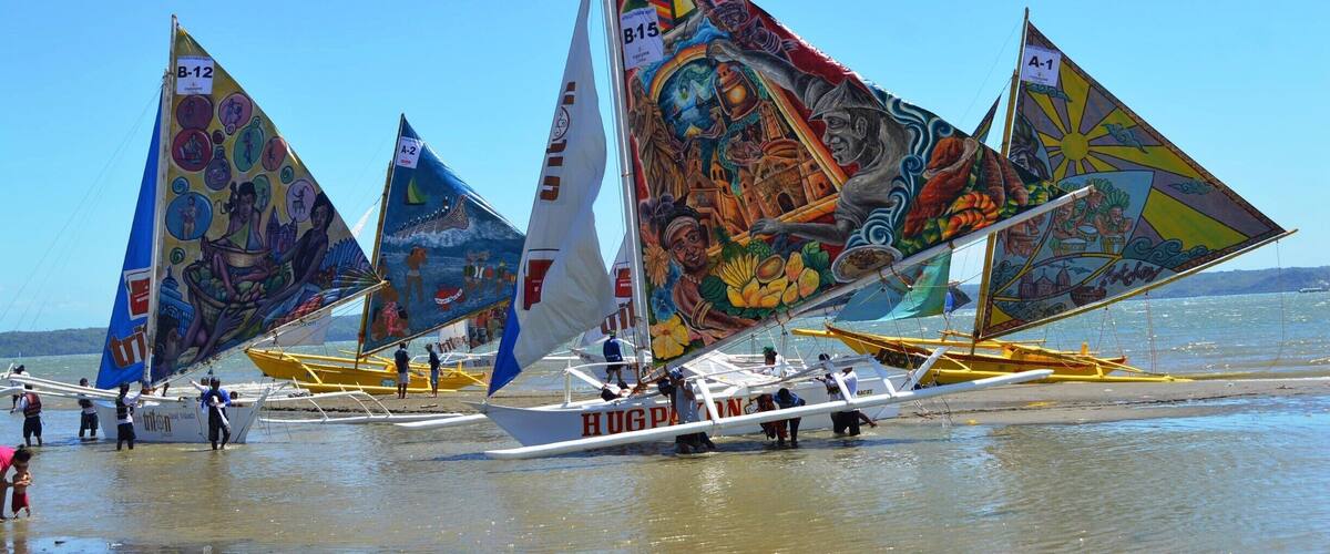 Colorful sailboats with intricate designs on their sails, docked on a beach.