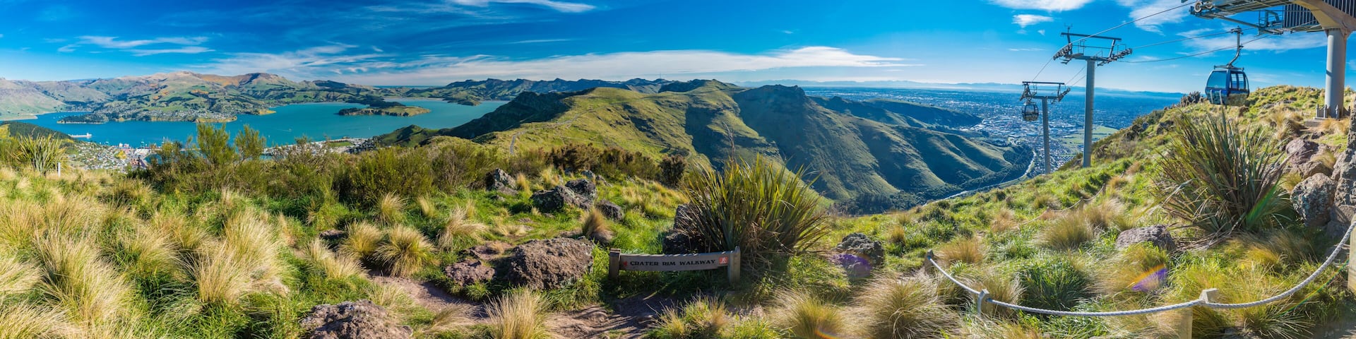 A mountainous landscape with a cable car system, a sign for Crater Rim Walkway, and a lake in the distance.