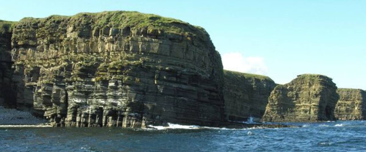 A coastal cliff with layered rock formations and a clear sky.