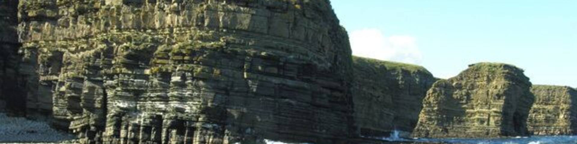 A coastal cliff with layered rock formations and a clear sky.