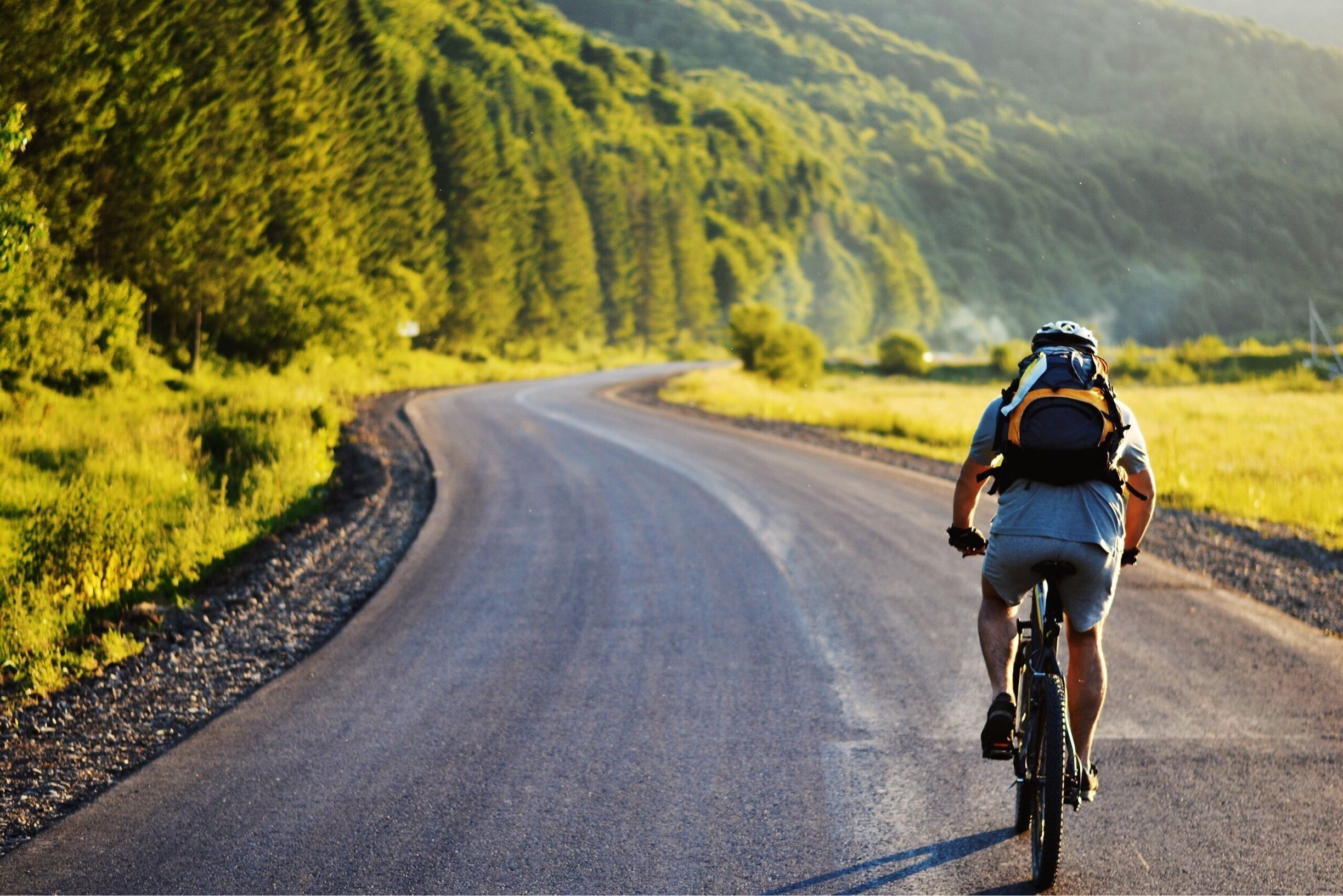 A cyclist on a winding road surrounded by lush greenery and hills.
