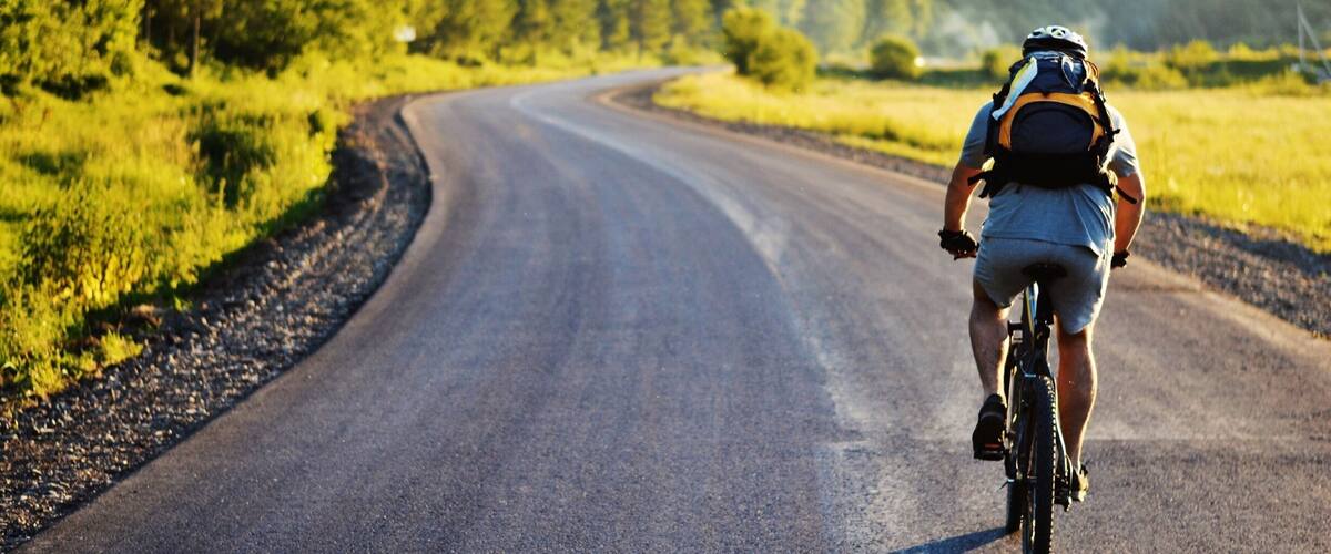 A cyclist on a winding road surrounded by lush greenery and hills.