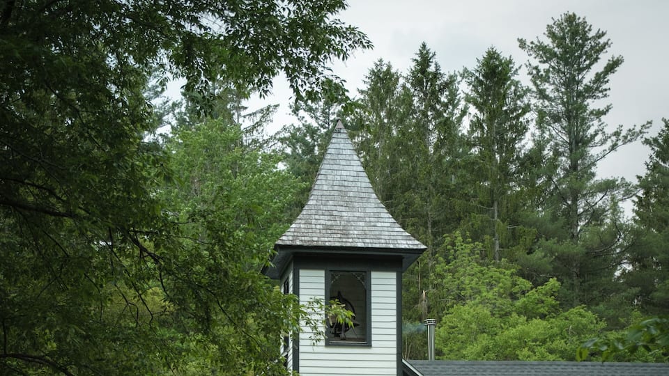 A white church with a bell tower, surrounded by trees.
