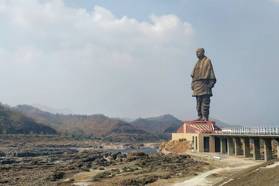 A large statue on a pedestal with a bridge in the background.