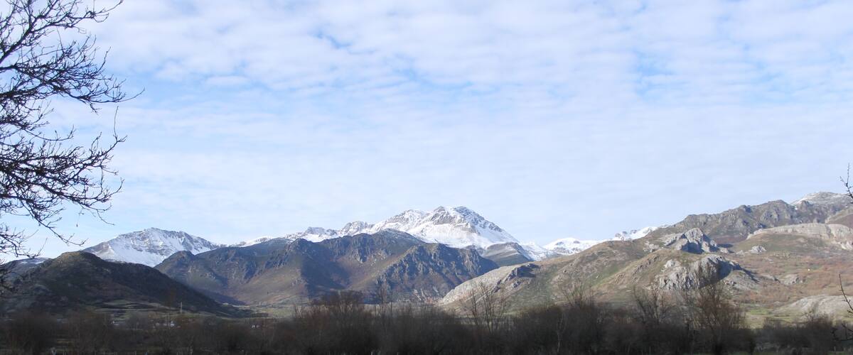 A stone wall, green field, and snow-capped mountains.