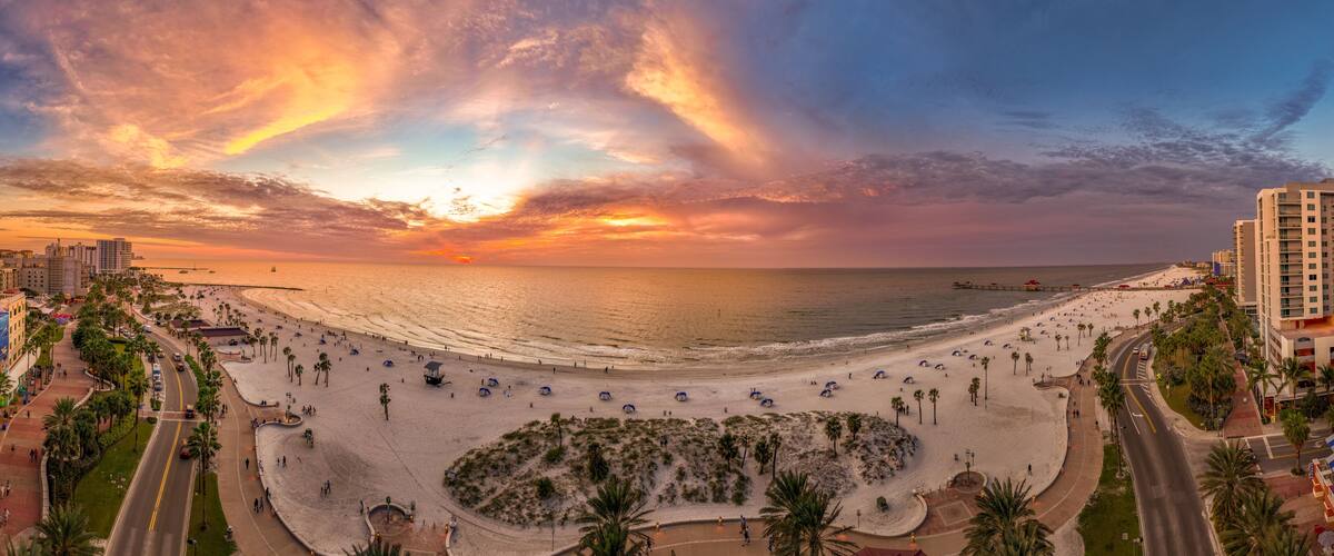 Ein Strand mit Palmen, einer Promenade und einem Sonnenuntergang.