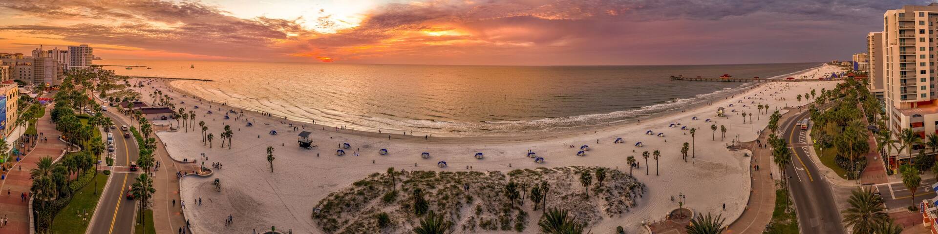 A beach with palm trees, a promenade, and a sunset.