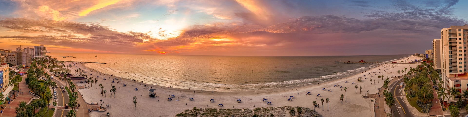 Ein Strand mit Palmen, einer Promenade und einem Sonnenuntergang.