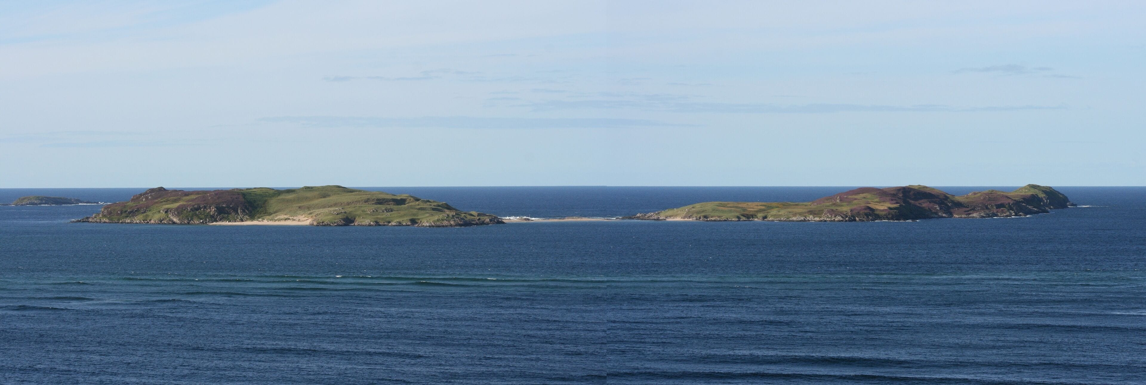 A coastal landscape with two green hills and a sandy beach.