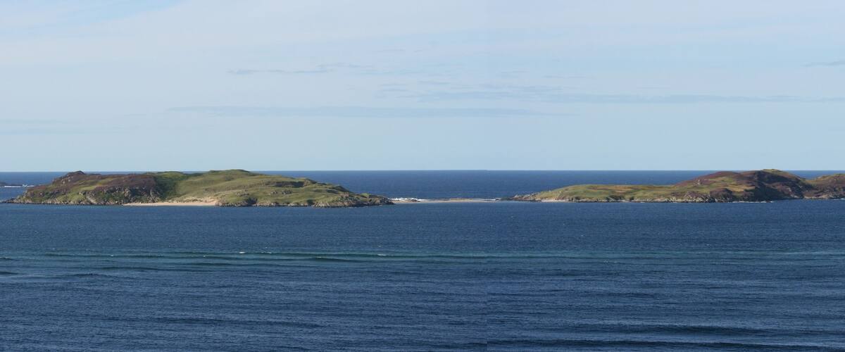 A coastal landscape with two green hills and a sandy beach.