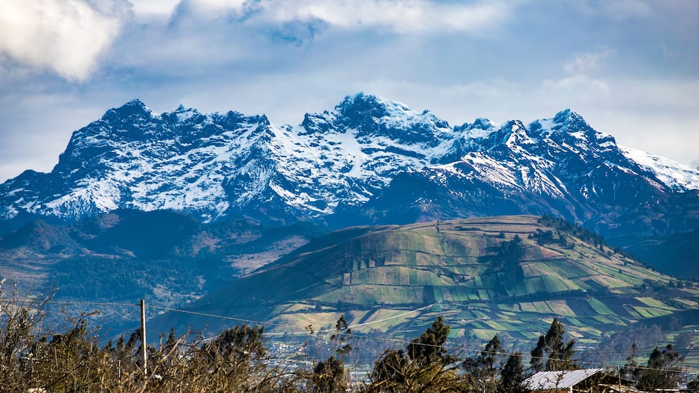 Snow-capped mountains, a valley with fields, and a distant house.
