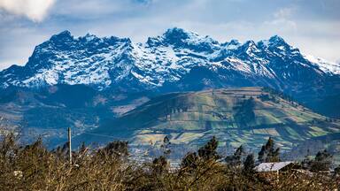 Snow-capped mountains, a valley with fields, and a distant house.