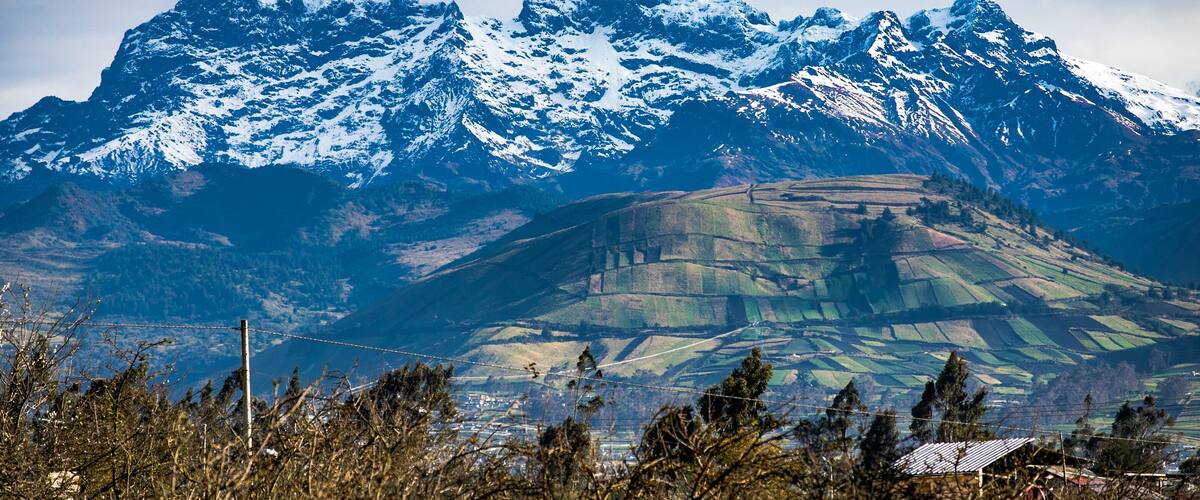 Snow-capped mountains, a valley with fields, and a distant house.