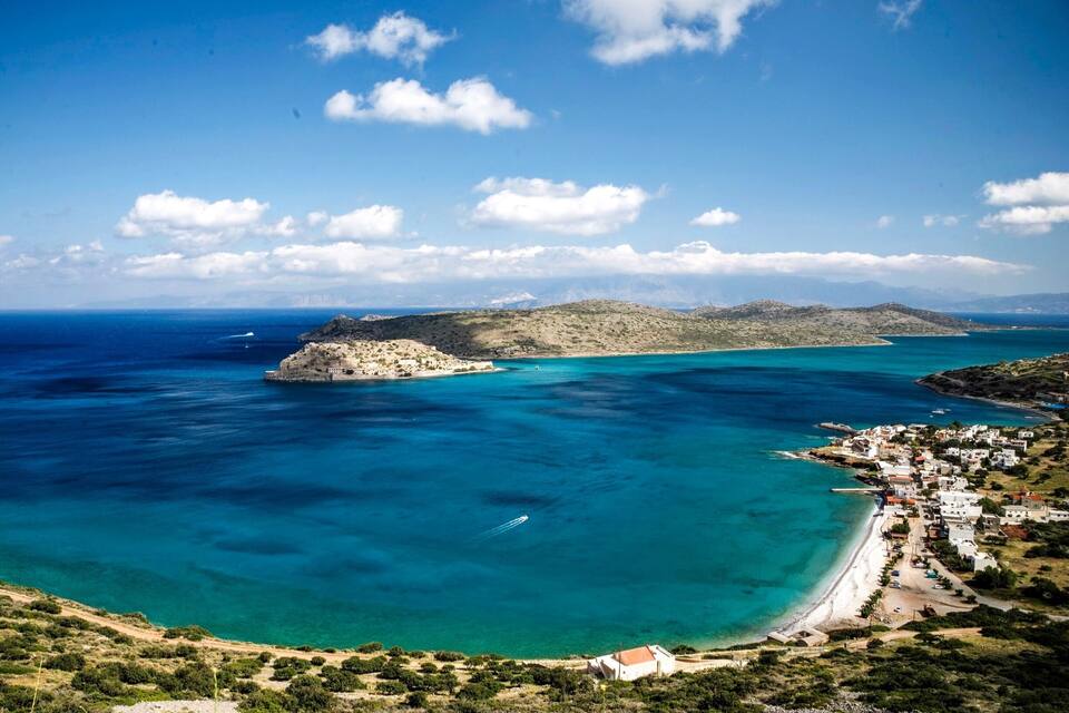 Un pueblo costero con aguas turquesas cristalinas, una pequeña isla y un telón de fondo montañoso.