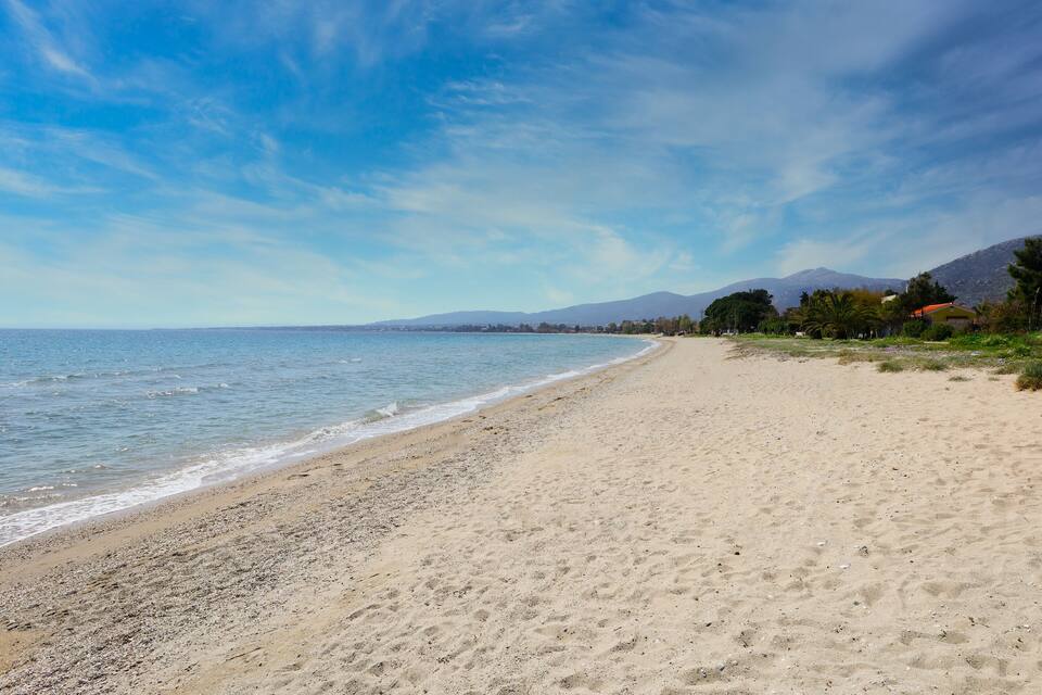A sandy beach with gentle waves, a clear sky, and distant mountains.