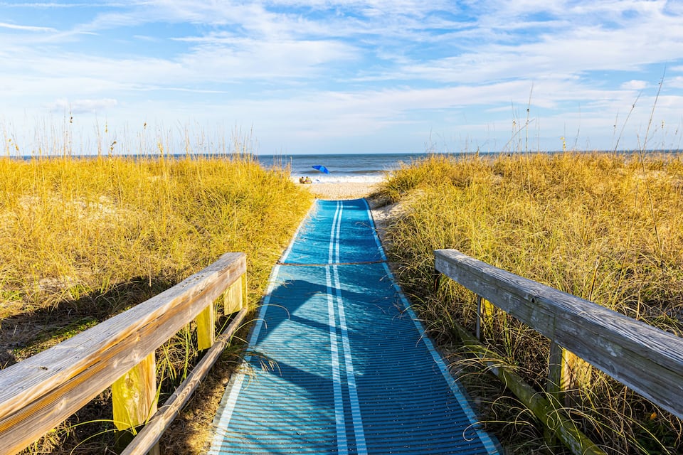 A wooden boardwalk leading to a beach with a clear blue sky.