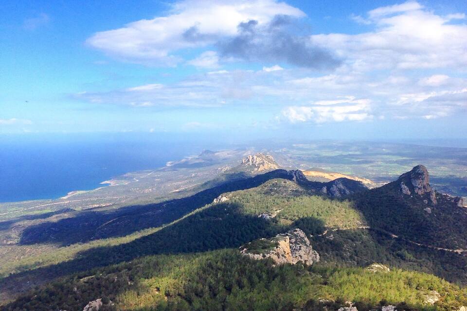 A mountainous landscape with a prominent peak and a coastal view in the distance.