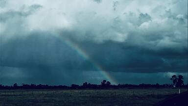 A stormy sky with a rainbow over a rural landscape.
