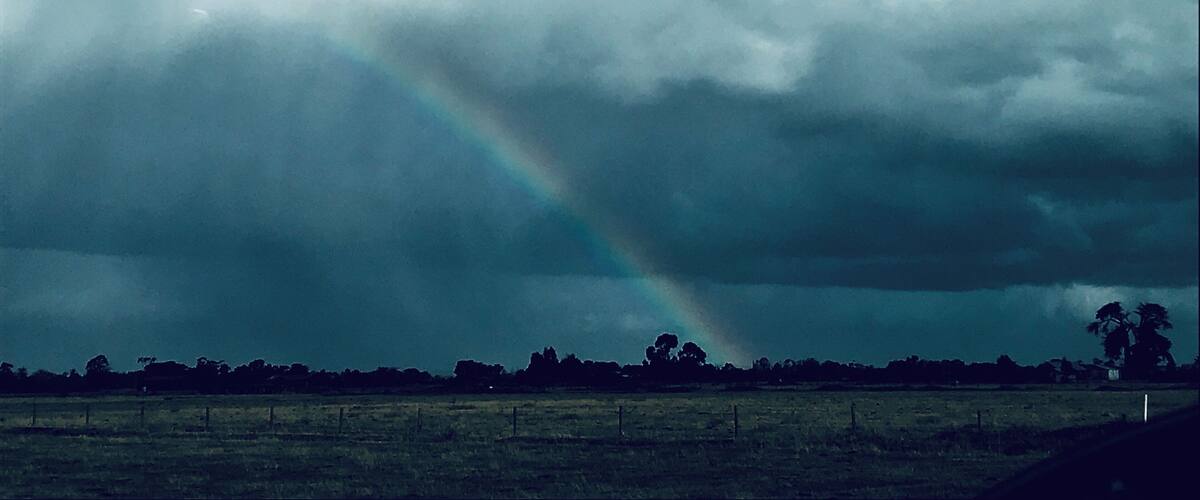 A stormy sky with a rainbow over a rural landscape.
