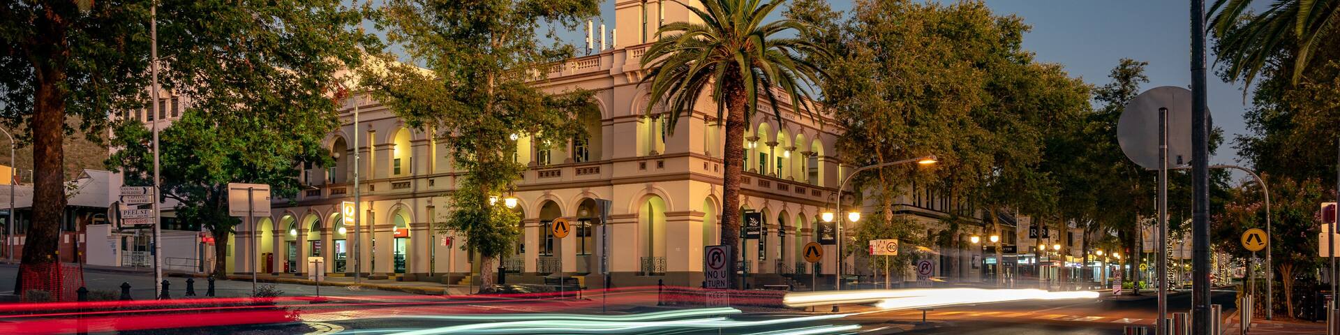 A historic building with a clock tower, palm trees, and a well-lit street at dusk.