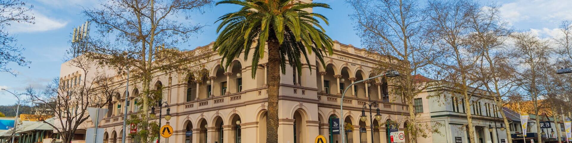 A historic building with a clock tower, palm trees, and a street with cars.