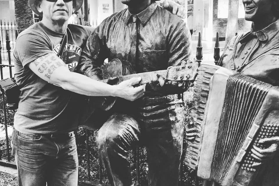 A person interacting with a statue of a man playing a guitar.