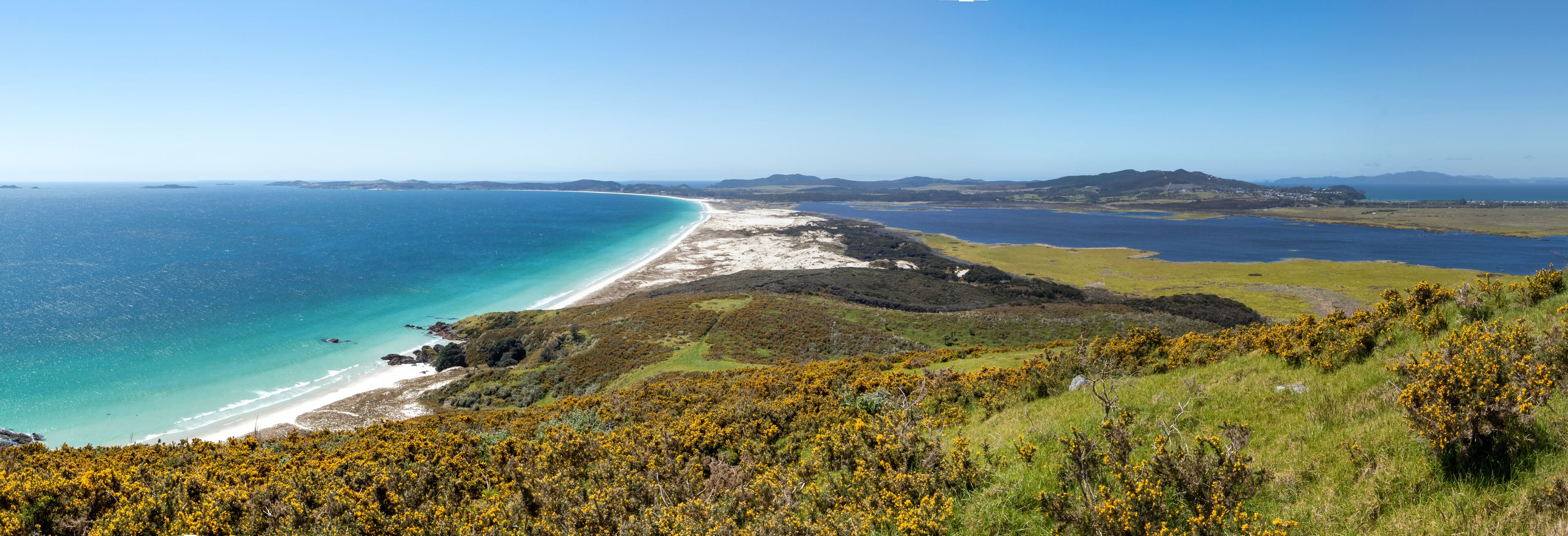 A coastal landscape with a beach, grassy hills, and distant mountains.