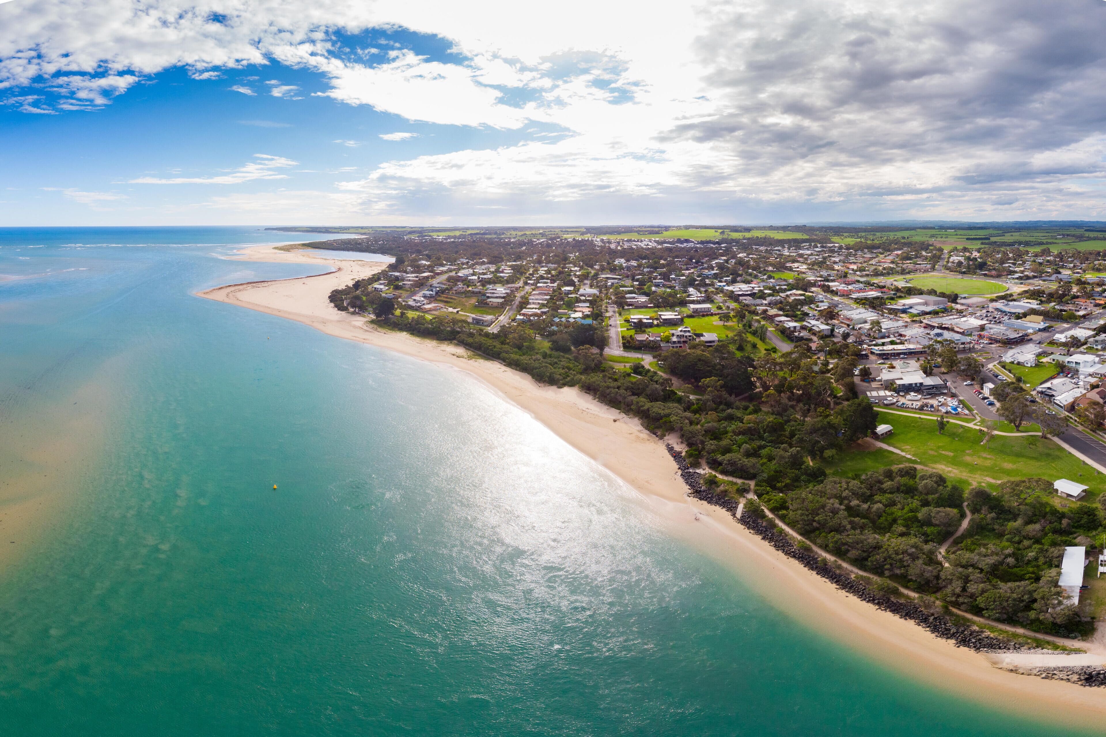 A coastal town with a beach, houses, and greenery.