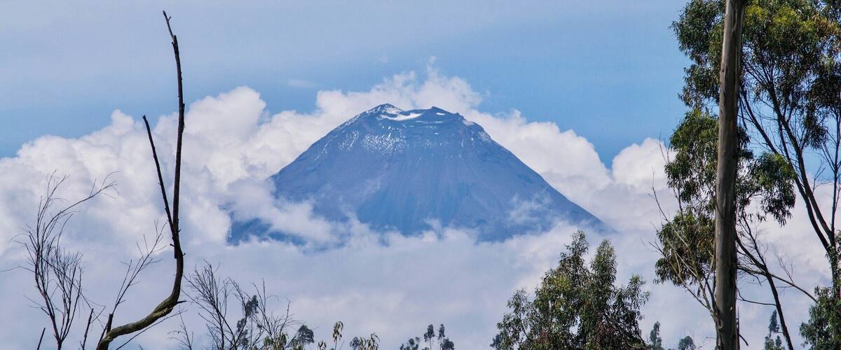 A mountain with a snow-capped peak, surrounded by clouds and trees.